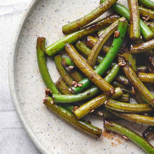 Sautéed garlic scapes in a pan with a glossy soy and sesame glaze
