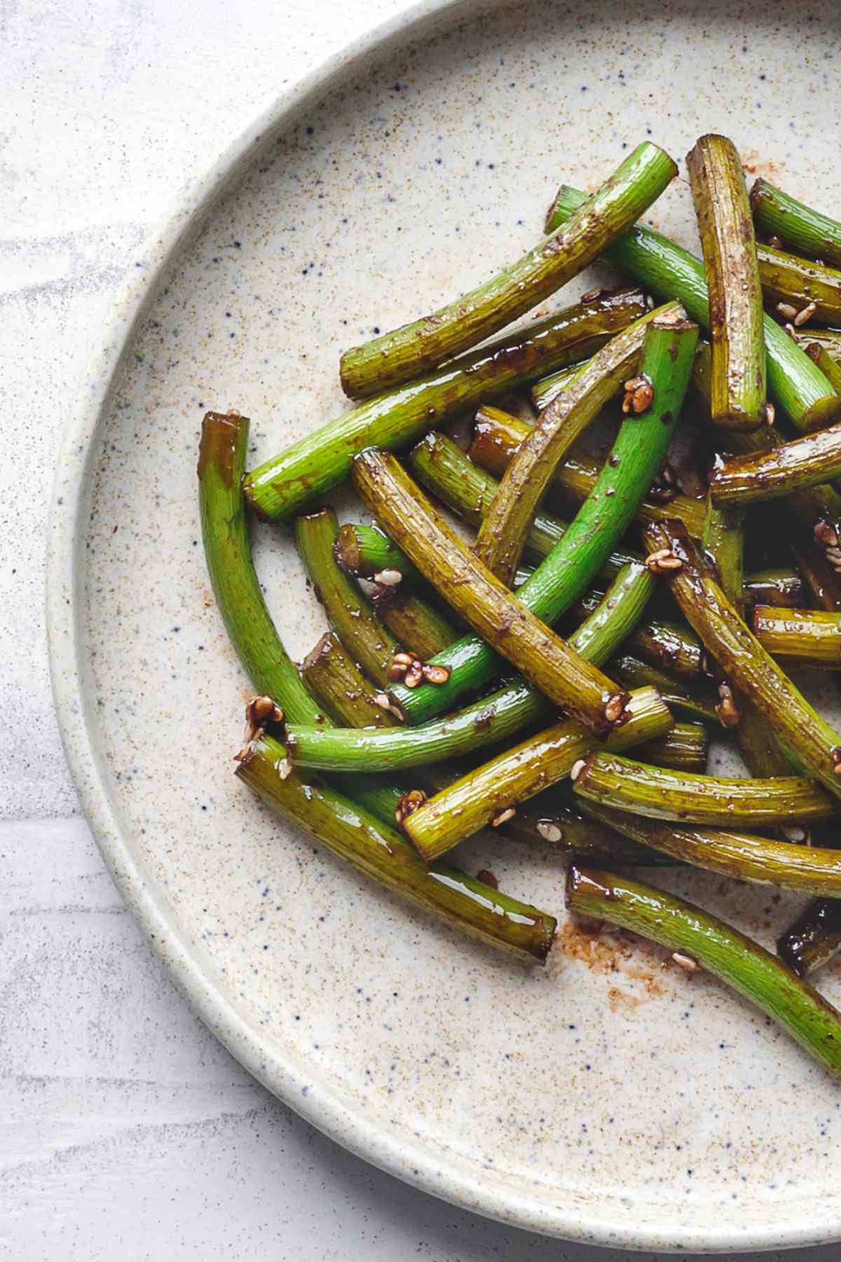 Sautéed garlic scapes in a pan with a glossy soy and sesame glaze