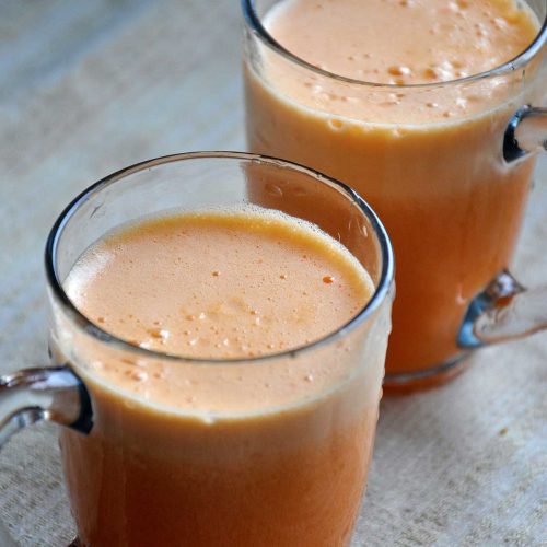 Two glass mugs of fresh frothy apricot juice