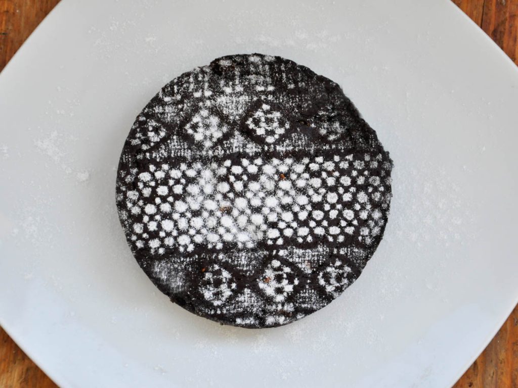 Whole vegan chocolate cake with a powdered-sugar lace top
