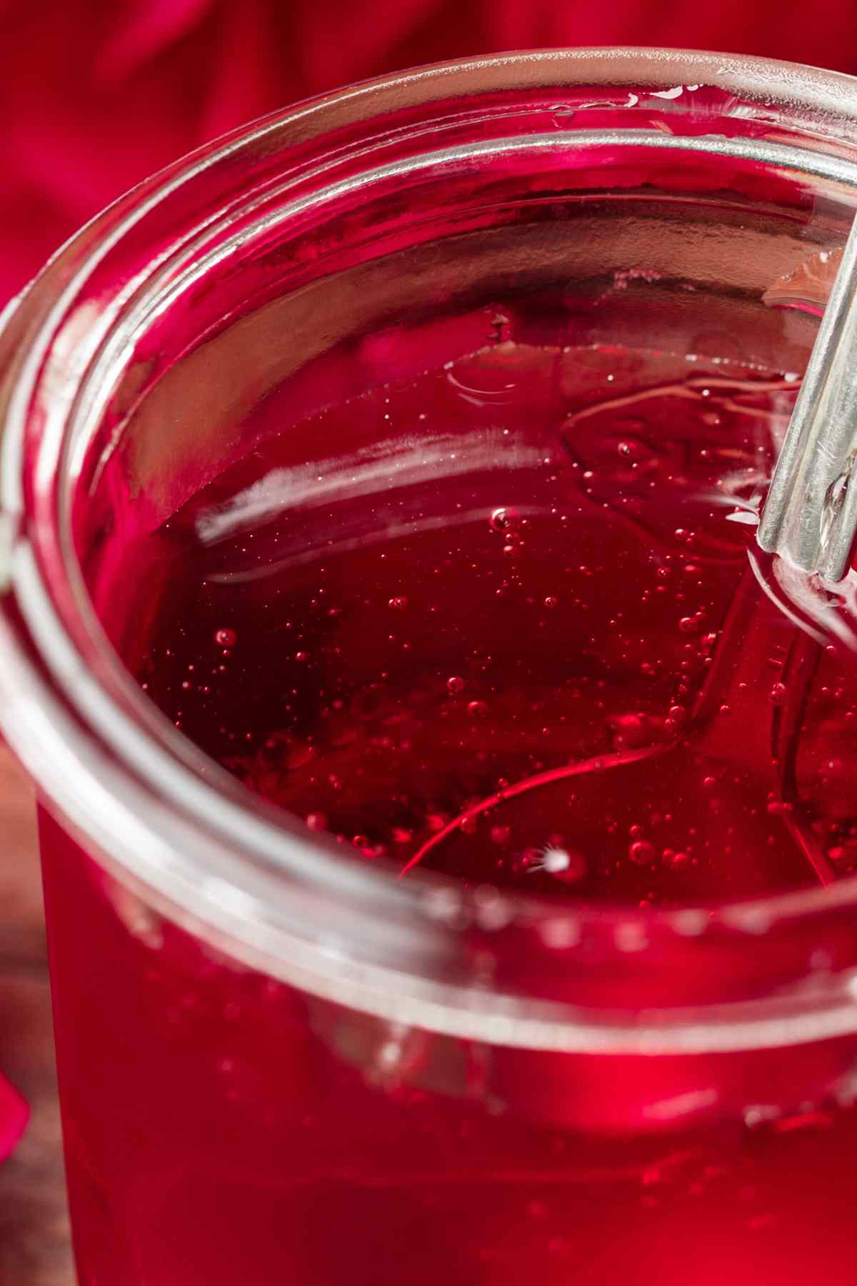 Jar of clear ruby-red rose jelly with a spoon