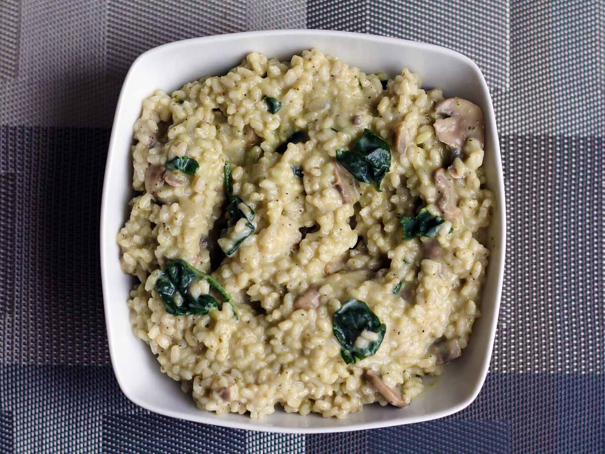 Creamy mushroom and spinach risotto in a white bowl, overhead