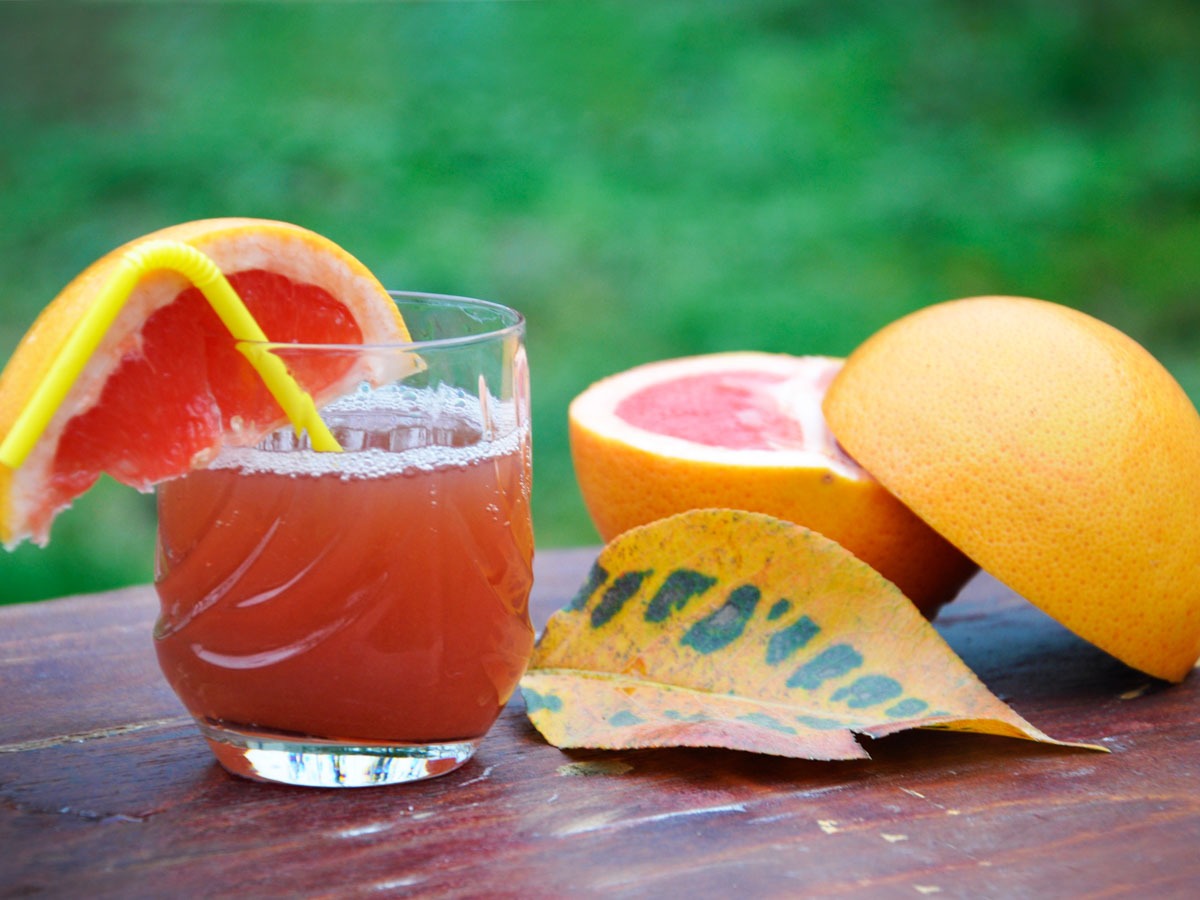 Pink grapefruit and strawberry juice in a glass, halved grapefruit behind