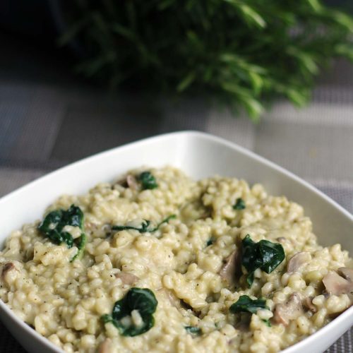 Vegetarian mushroom risotto with spinach in a white bowl, rosemary behind