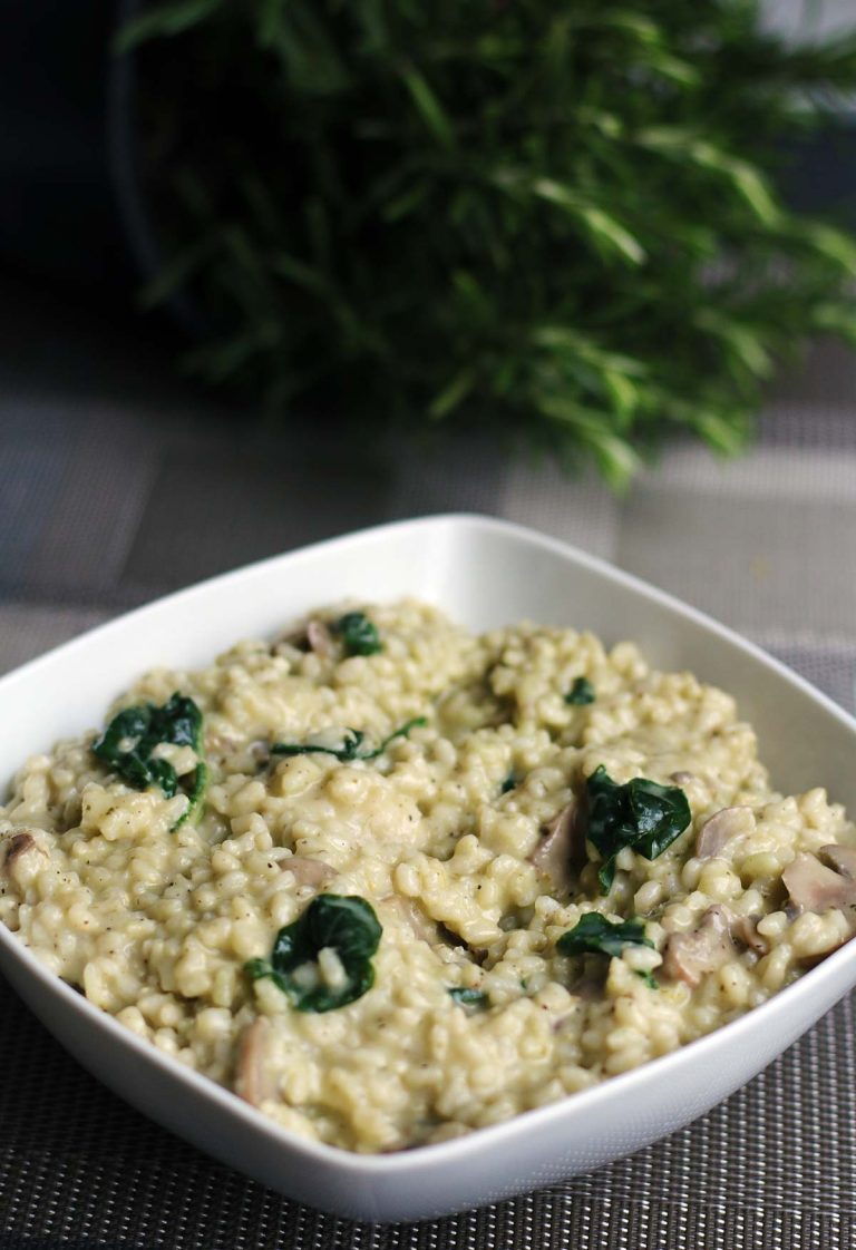 Vegetarian mushroom risotto with spinach in a white bowl, rosemary behind