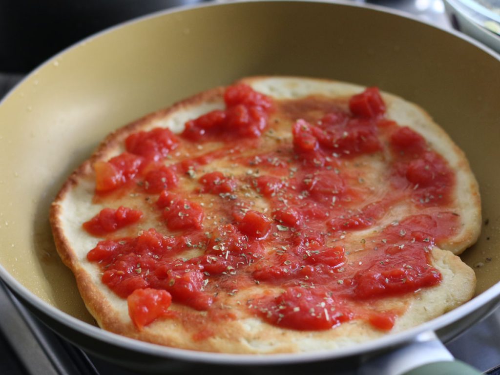Spreading tomato sauce on the cooked pizza base