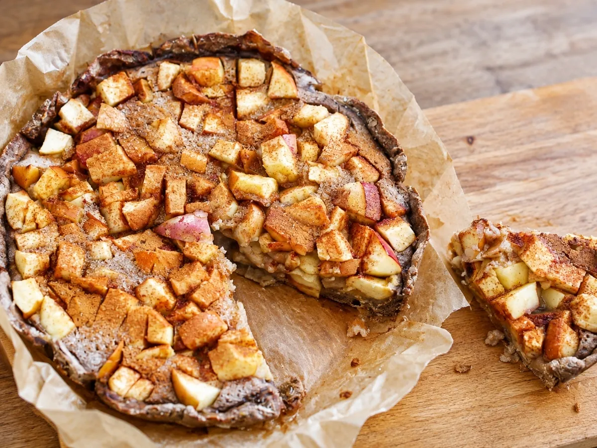 Apple custard tart with one slice cut and pulled away on parchment