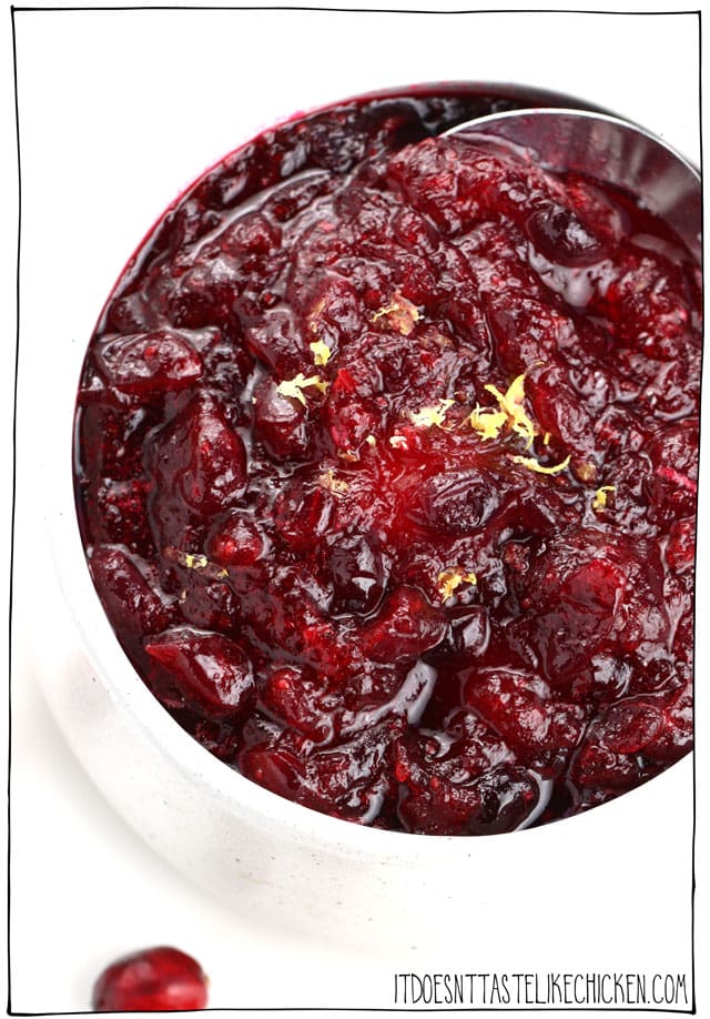 Glossy homemade vegan cranberry sauce in a white bowl with a spoon, topped with fresh lemon zest.