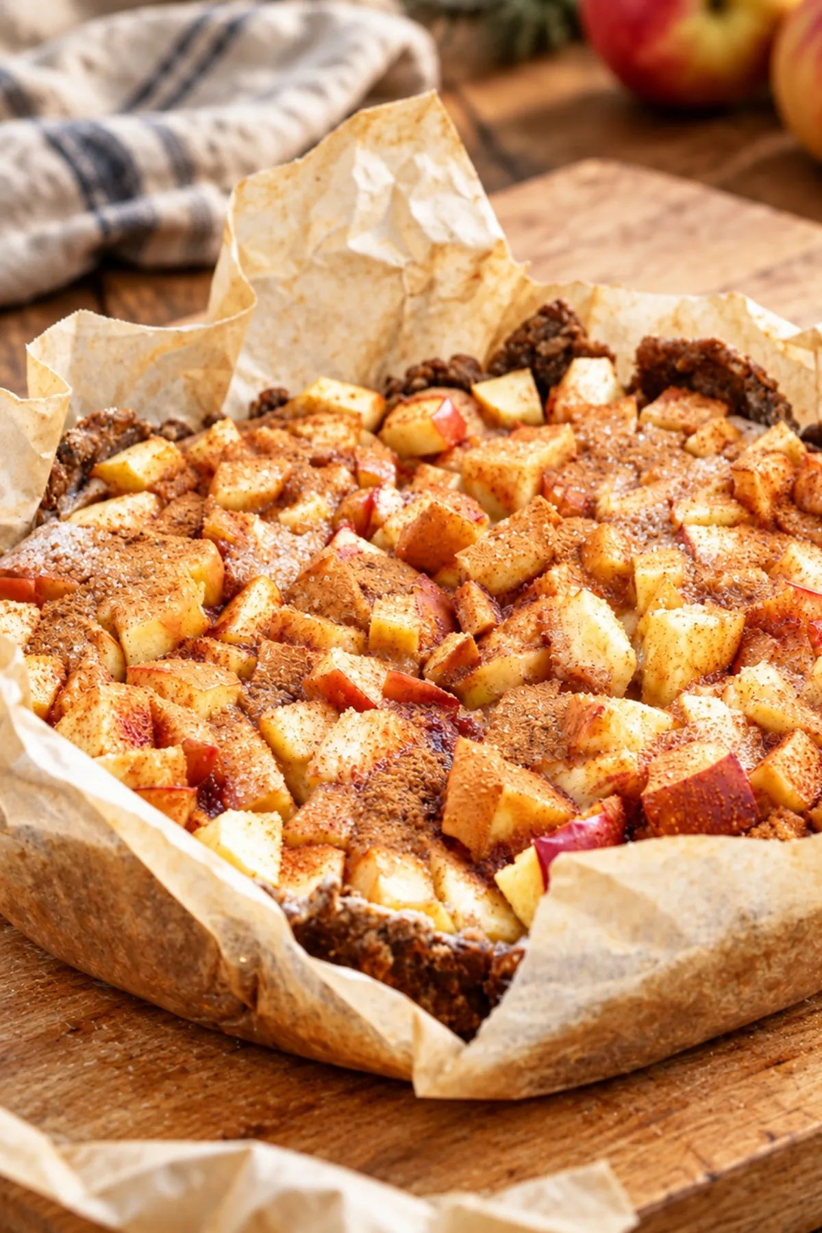 Whole wheat apple custard tart topped with cinnamon-dusted apple cubes, in crumpled parchment with red apples behind